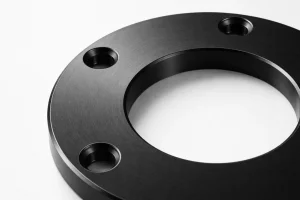 Close-up of a black anodized aluminum flange showing smooth machined surface and bolt holes